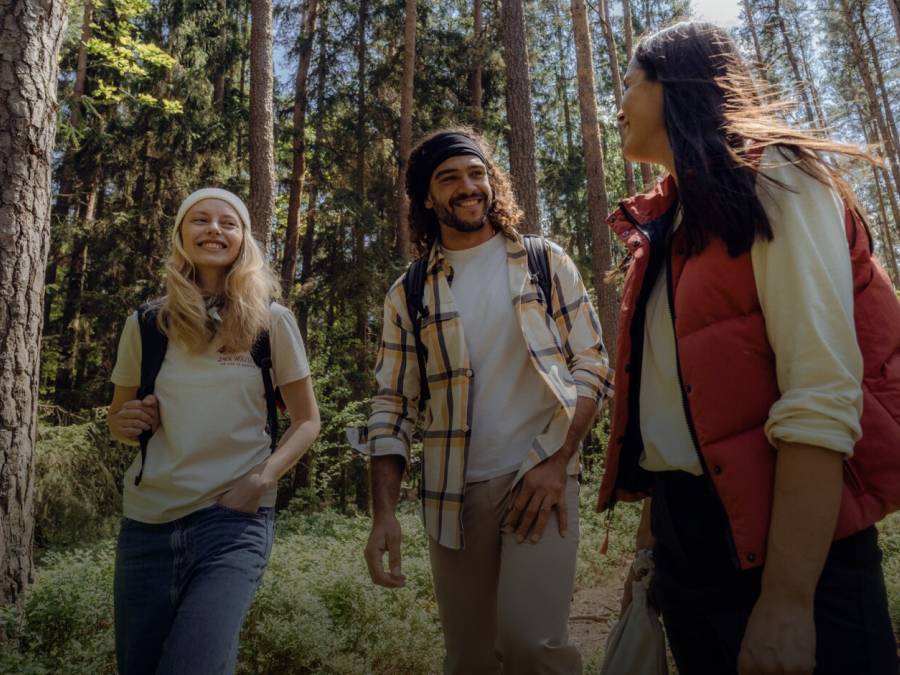 Drie lachende wandelaars in casual herfst wandelkleding in het zonnige bos