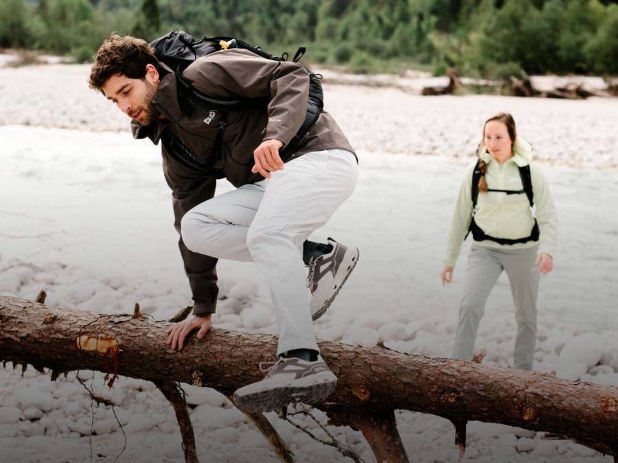 Jonge man in wandelkleding springt over een boomstam